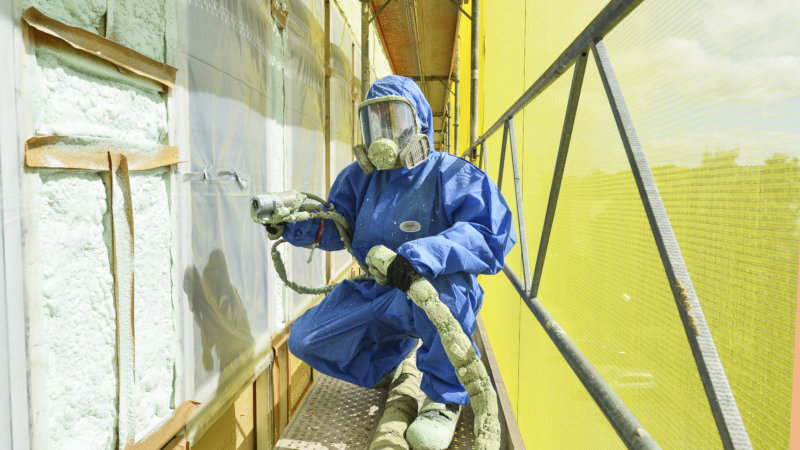 Man i skyddsutrustning sprayar isolering i vägg.