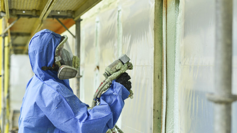 Man i skyddsutrusting sprayar isolering på en vägg.